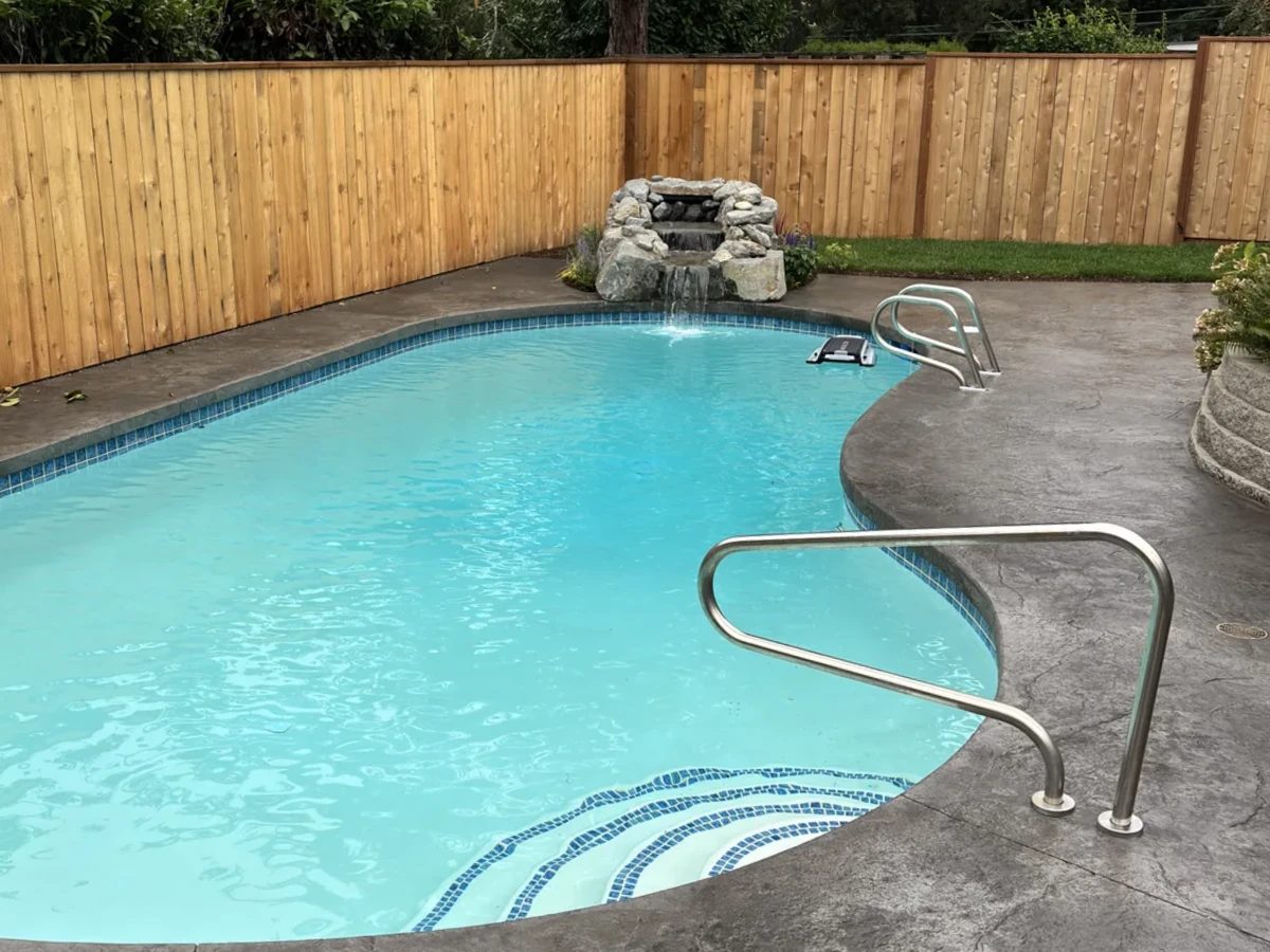 Finished pool renovation with new tile, stamped concrete deck, cedar privacy fence, and rock waterfall